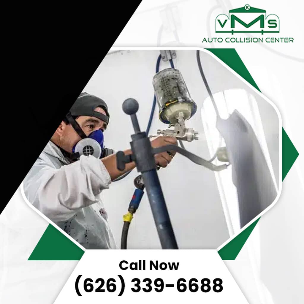 An auto body technician wearing a protective respirator spraying paint onto a car panel inside a paint booth.